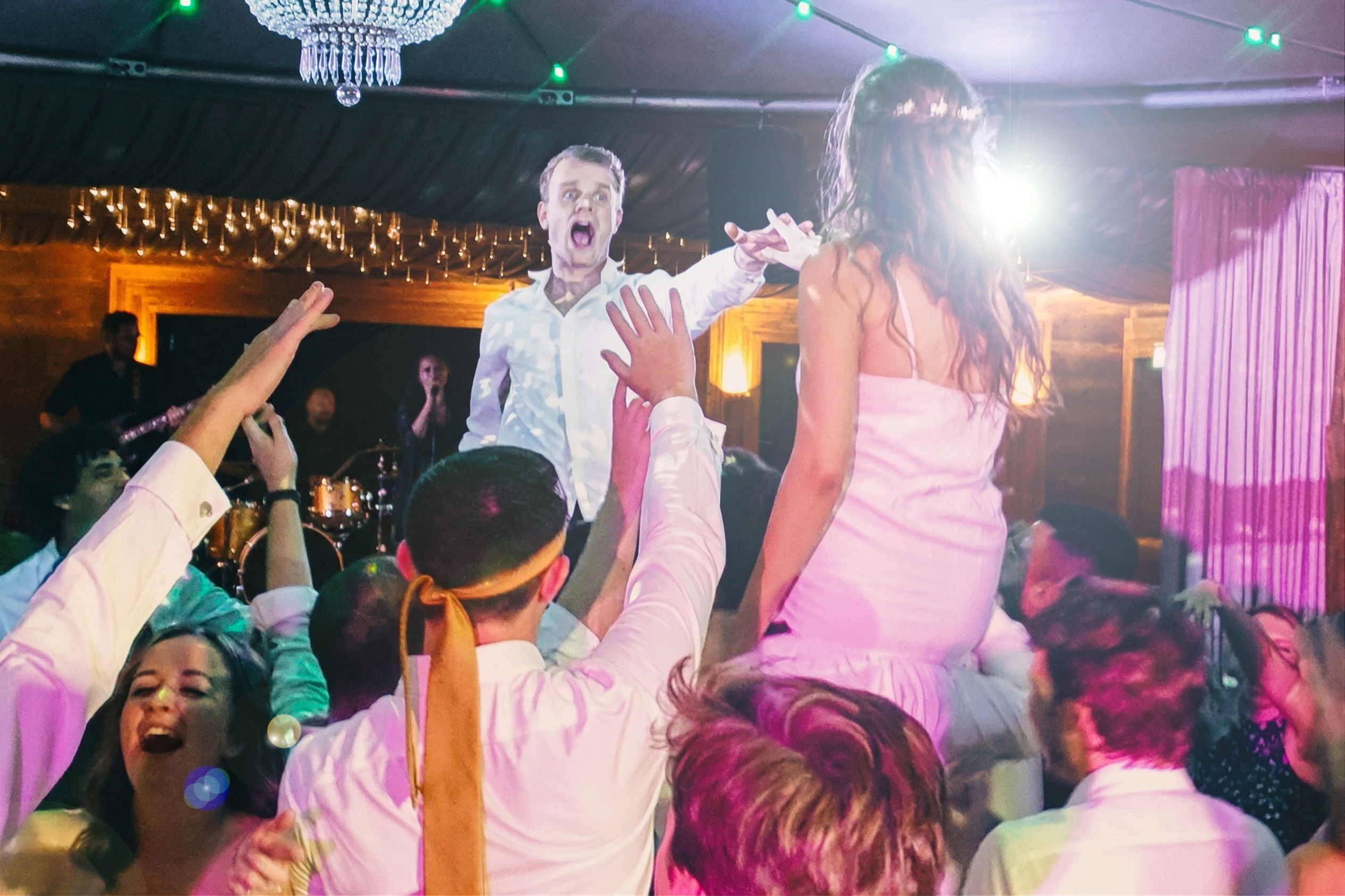 Packed dancefloor with wedding band playing live, bride and groom on guests shoulders